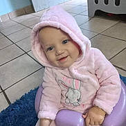 Vinay joined the competition — help win amazing prizes! baby, child, toddler, portrait, smiling, happy, pink_outfit, hooded_clothing, bunny_design, seated, chair, purple_chair, blue_rug, indoor, home, tiled_floor, laundry_basket, face, hands, social_media_screenshot