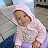 baby, child, toddler, portrait, smiling, happy, pink_outfit, hooded_clothing, bunny_design, seated, chair, purple_chair, blue_rug, indoor, home, tiled_floor, laundry_basket, face, hands, social_media_screenshot