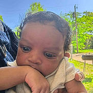 Ca'Juan is registered to the contest to win money with this photo: baby, child, infant, close_up, outdoor, daylight, hand, arm, person, skin, face, curly_hair, blue_sky, greenery, trees, holding, thoughtful, casual_clothing, nature, sunlight