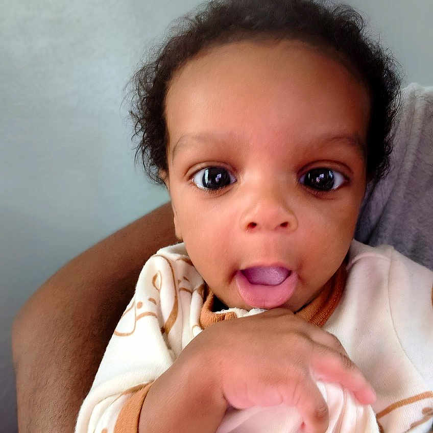 Ca'Juan joined the competition — help win amazing prizes! baby, child, infant, face, eyes, pajamas, hand, armchair, expression, tongue, person, indoor, cute, young, skin, clothing, portrait, curly_hair, holding, comfortable