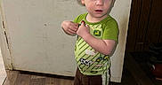 Greyson joined the competition — help win amazing prizes! brown_pants, casual, child, clothing, curly_hair, door, doorknob, expression, flooring, footwear, green_shirt, home, indoor, person, scratched_door, standing, toddler, wall, wood_floor, young_child