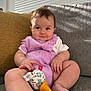 baby, infant, child, purple_outfit, rattle, toy, couch, sofa, cushion, indoor, natural_light, curtains, window_blinds, skin, legs, hands, face, smile, seated, cute