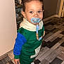 Paolo Greco participe au concours pour gagner de l'argent avec cette photo : toddler, child, pacifier, clothing, indoor, floor, patterned_floor, person, shoes, toy, hair, blue, green, white, sneakers, standing, holding, wall, cabinet, cute