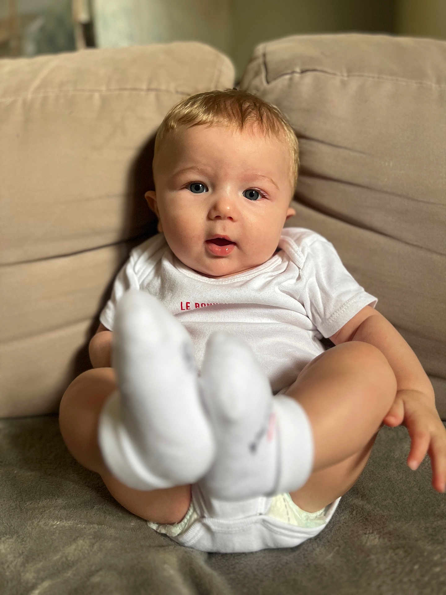 Kaylan participe au concours pour gagner de l'argent avec cette photo : baby, infant, child, couch, socks, onesie, blonde_hair, blue_eyes, indoor, portrait, cute, seated, soft_lighting, closeup, expression, comfort, home, person, skin, feet