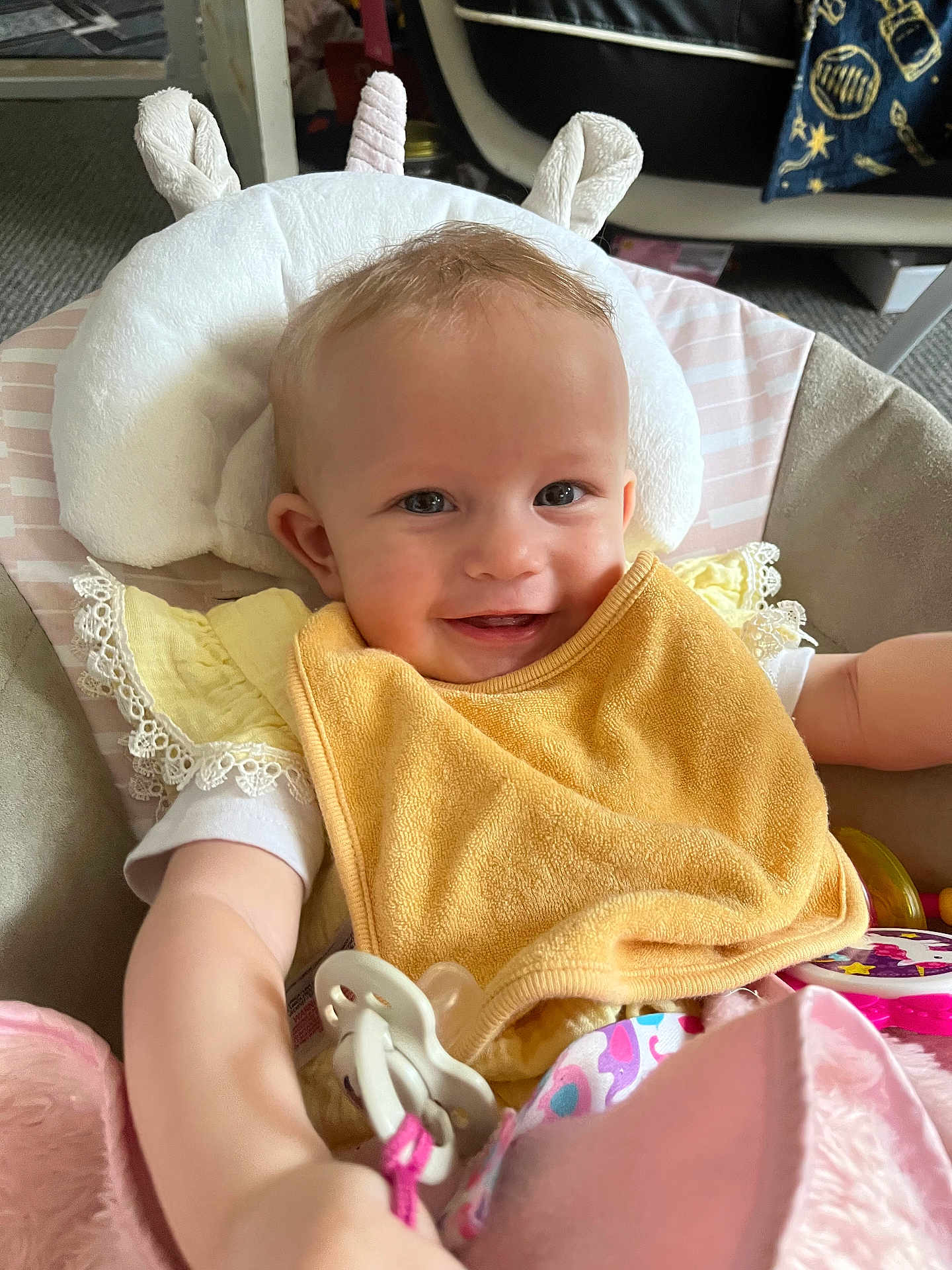 Arabella joined the competition — help win amazing prizes! baby, smiling, bib, pacifier, cushion, soft_toy, indoor, child, cute, seated, yellow, clothing, infant, face, headrest, playful, happy, portrait, comfort, toy