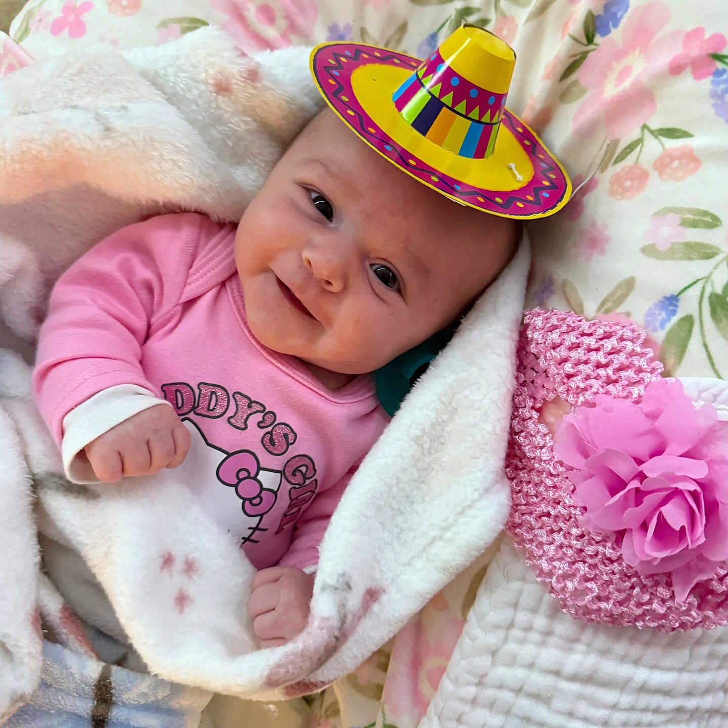 Savannah Casey is registered to the contest to win money with this photo: baby, bedspread, blanket, bottle, child, cozy, cute, cute_accessory, floral_pattern, happy, indoors, infant, knitted_hat, lying_down, pink_clothing, pink_flower, portrait, smiling, soft_texture, sombrero