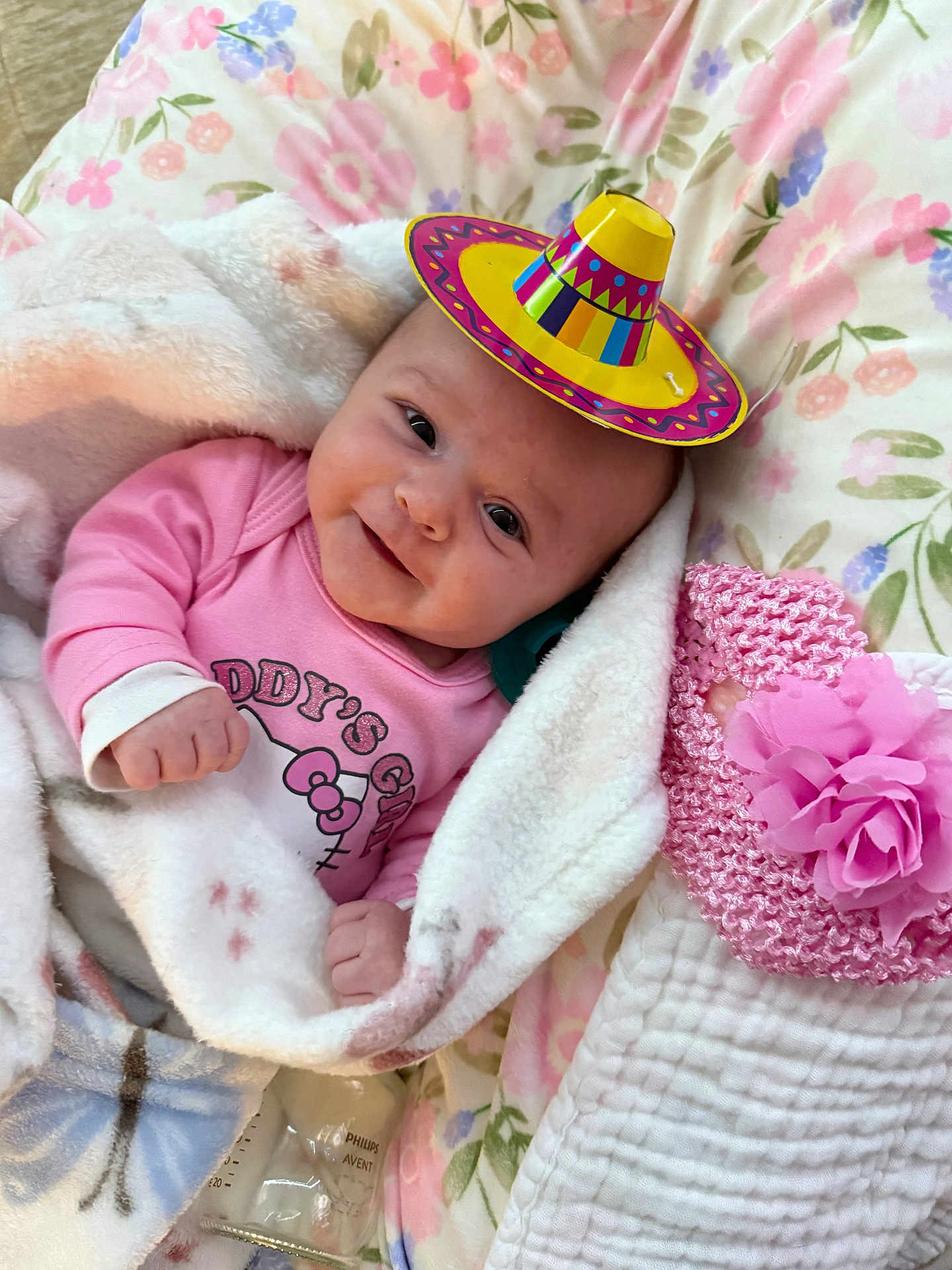 Savannah Casey is registered to the contest to win money with this photo: baby, smiling, blanket, pink_clothing, sombrero, floral_pattern, bedspread, pink_flower, knitted_hat, soft_texture, infant, cute, indoors, lying_down, cozy, portrait, child, happy, cute_accessory, bottle