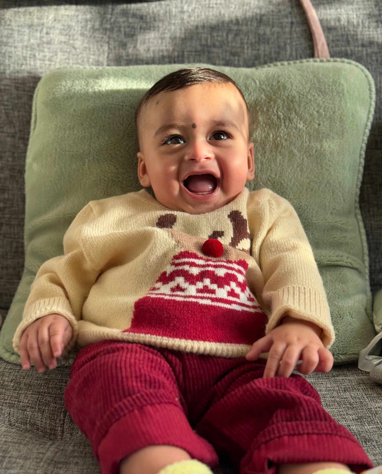 Avighna joined the competition — help win amazing prizes! baby, child, smiling, sitting, sweater, red_pants, pom_pom, couch, cushion, indoor, happy, cute, face, portrait, hands, clothing, cozy, infant, person, warm