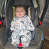 baby, car_seat, infant, onesie, mickey_mouse, child, floor, wooden_floor, seatbelt, strapped_in, indoor, cute, clothing, person, young_child, car_seat_interior, baby_girl, baby_boy, sitting, expression
