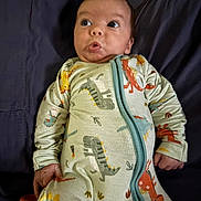 Camden is registered to the contest to win money with this photo: baby, infant, onesie, dinosaur_print, pacifier, clothing, bed, fabric, expression, hand, face, cute, child, lying_down, newborn, sleepwear, portrait, indoors, soft_lighting, person