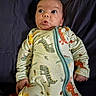 baby, infant, onesie, dinosaur_print, pacifier, clothing, bed, fabric, expression, hand, face, cute, child, lying_down, newborn, sleepwear, portrait, indoors, soft_lighting, person