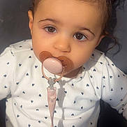 Lya a rejoint le concours — aidez-le/la à gagner de superbes lots ! baby, child, pacifier, pacifier_clip, hair_buns, hair_accessory, pink_bows, brown_eyes, onesie, heart_pattern, close_up, portrait, adorable, sitting, indoor, cute, infant, toddler, sticker_hearts, soft_lighting