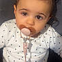 baby, child, pacifier, pacifier_clip, hair_buns, hair_accessory, pink_bows, brown_eyes, onesie, heart_pattern, close_up, portrait, adorable, sitting, indoor, cute, infant, toddler, sticker_hearts, soft_lighting