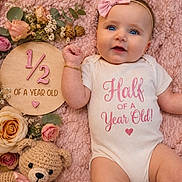 Elianna joined the competition — help win amazing prizes! baby, infant, child, portrait, smiling, blue_eyes, pink_blanket, hair_bow, white_onesie, milestone_photo, six_months, flowers, rose, bouquet, teddy_bear, wooden_sign, indoor, lying_down, pastel, birthday