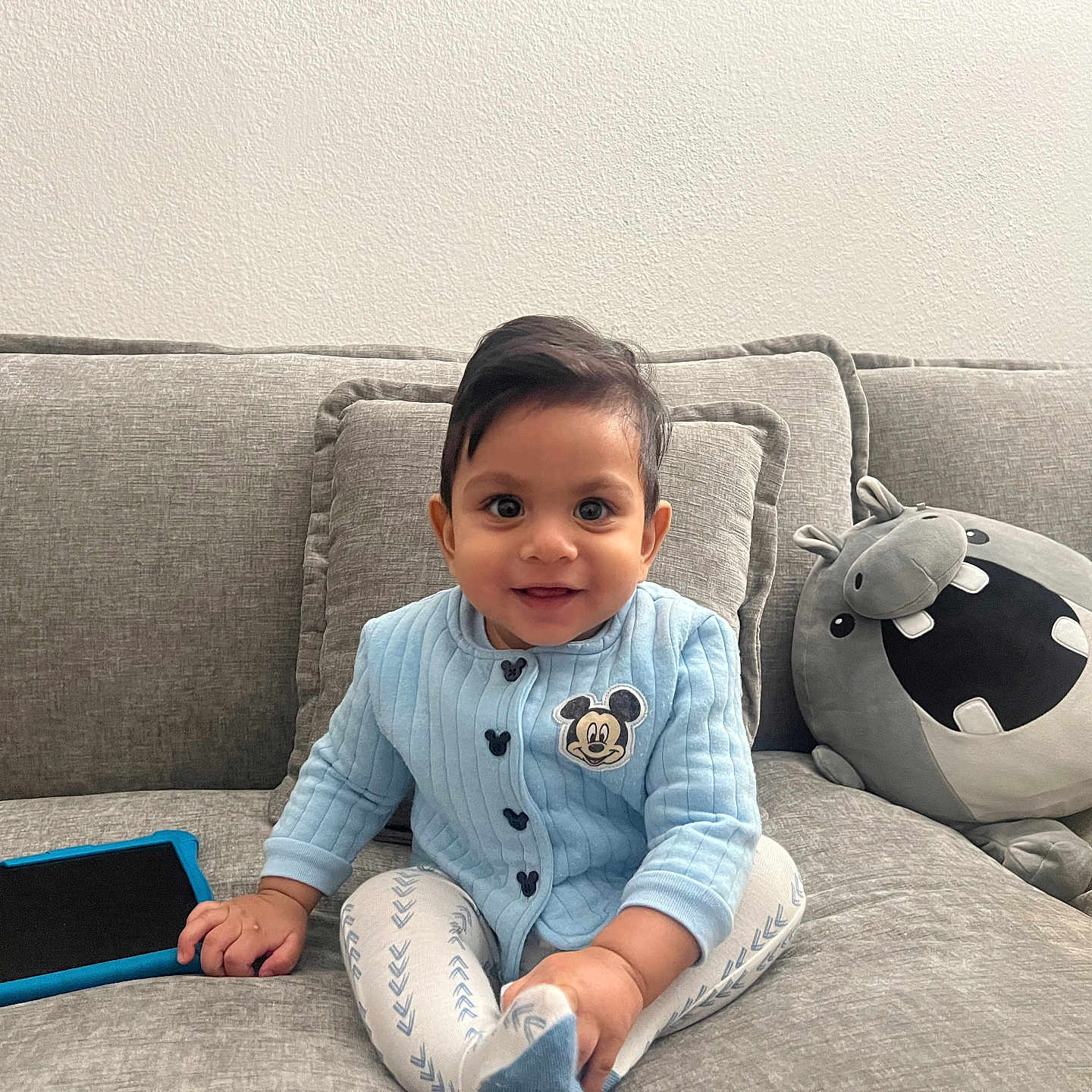Ezhaan is registered to the contest to win money with this photo: baby, blue_sweater, casual, child, couch, cozy, cute, face, gray_cushions, happy, home, indoor, mickey_mouse, person, plush_hippo, sitting, smiling, soft_lighting, tablet, yellow_cap