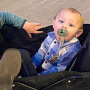 Jacob is registered to the contest to win money with this photo: toddler, child, pacifier, stroller, hand, blue_clothing, casual_wear, curious_expression, outdoor, pavement, footwear, baby, person, seat, jacket, young_child, infant, cute, portrait, casual
