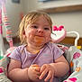 Savannah-Rae is registered to the contest to win money with this photo: baby, child, messy, food, highchair, purple_shirt, tulip_print, hands, face, smile, indoor, blurred_background, cute, infant, seated, playful, young_child, happy, colorful, feeding_time