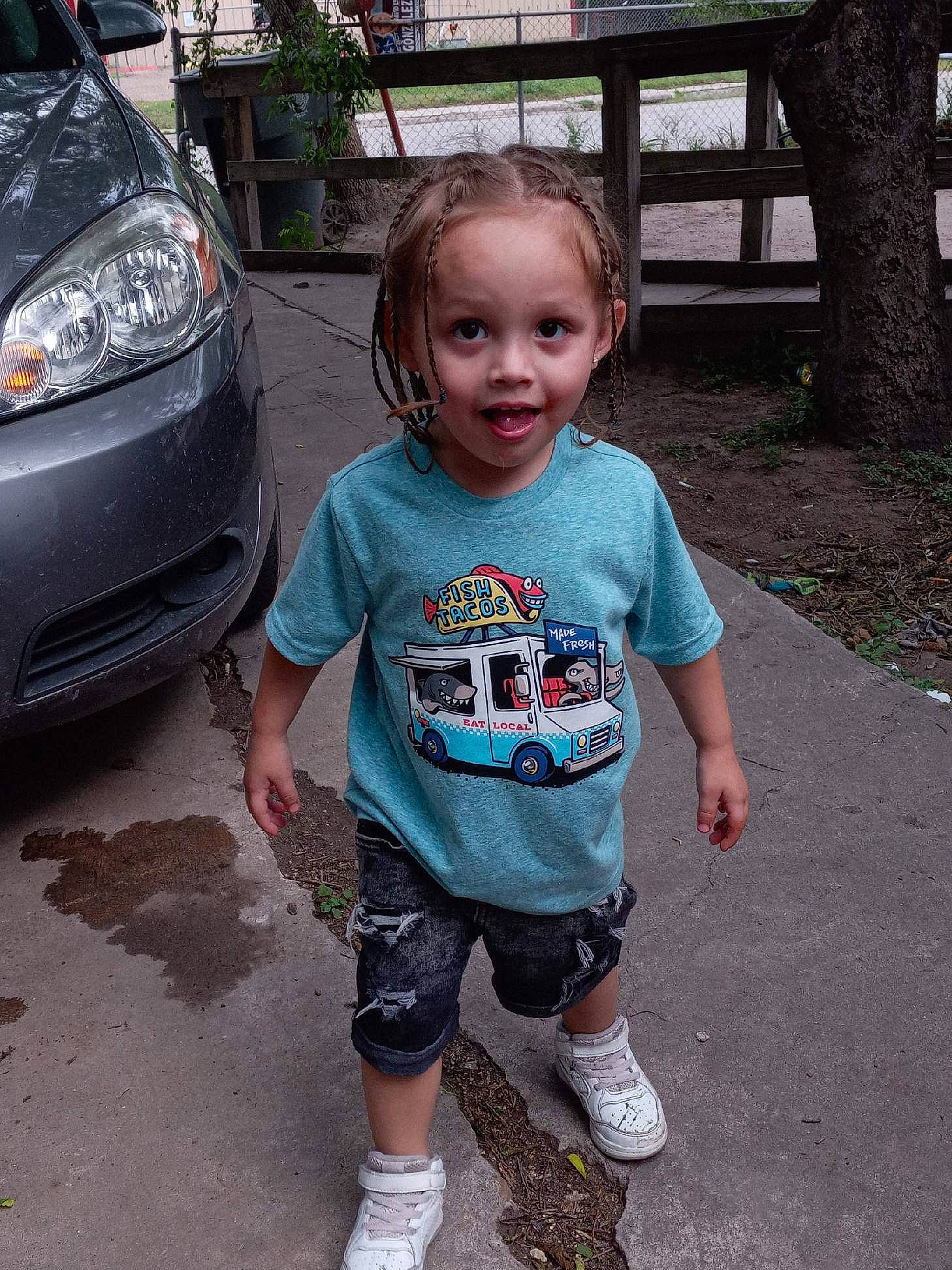 Dallas is registered to the contest to win money with this photo: automotive_design, automotive_exterior, automotive_lighting, automotive_tire, bumper, car, fender, grille, happy, hood, motor_vehicle, person, plant, shoe, sleeve, sneakers, toddler, tree, trunk, vehicle