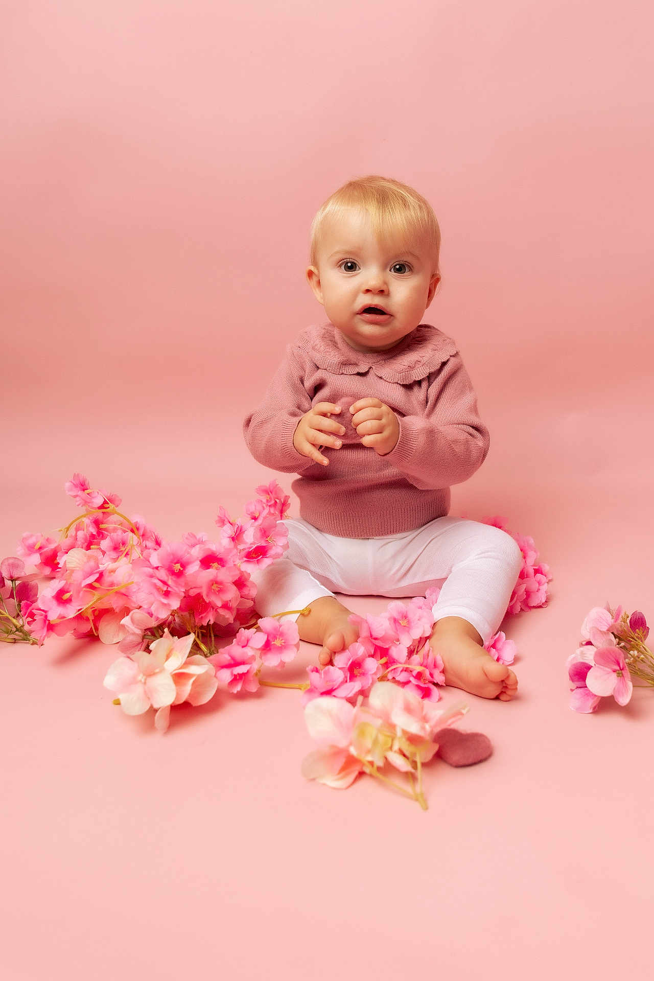 Julya participe au concours pour gagner de l'argent avec cette photo : baby, child, pink_background, pink_sweater, white_leggings, flowers, sitting, portrait, cute, indoor, studio, infant, flower_petals, soft_lighting, looking_at_camera, barefoot, blond_hair, young_child, adorable, smiling