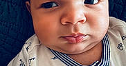 Hunter is registered to the contest to win money with this photo: baby, infant, face, expression, furrowed_brow, clothing, onesie, cartoon_print, dog_print, closeup, portrait, child, cute, skin, head, person, laying_down, blanket, textile, indoors