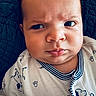 baby, infant, face, expression, furrowed_brow, clothing, onesie, cartoon_print, dog_print, closeup, portrait, child, cute, skin, head, person, laying_down, blanket, textile, indoors