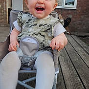 Arabella is registered to the contest to win money with this photo: baby, child, smiling, happy, mickey_mouse, dress, curly_hair, chair, outdoor, wooden_deck, building, window, door, person, tights, feet, hand, seatbelt, playful, young