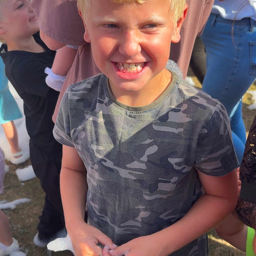 Corey is registered to the contest to win money with this photo: blond_hair, blue_shorts, boy, bubbles, camouflage_shirt, casual_clothing, child, children, daytime, foam, fun, grass, group, happy, outdoor, people, playful, smiling, summer, sunlight