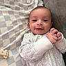 baby, infant, child, smiling, portrait, lying_down, hands, clasped_hands, blanket, checkered_blanket, couch, home, indoor, cozy, onesie, patterned_clothing, face, eyes, happy, photography