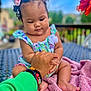baby, child, hand, bracelets, pink_bows, curly_hair, blanket, outdoor, table, flower, green_sleeve, skin, infant, holding_hand, person, cute, sitting, colorful, nature, portrait