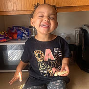 Iris is registered to the contest to win money with this photo: bodypart, cabinet, child, closet, clothing, face, female, furniture, girl, happy, head, mouth, pants, person, photography, portrait, sitting, t_shirt, teeth, wood