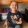 bodypart, cabinet, child, closet, clothing, face, female, furniture, girl, happy, head, mouth, pants, person, photography, portrait, sitting, t_shirt, teeth, wood
