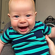 Colter joined the competition — help win amazing prizes! baby, child, smiling, indoor, person, clothing, striped_clothing, onesie, happy, face, head, skin, hand, leg, door, furniture, room, background, blue, green