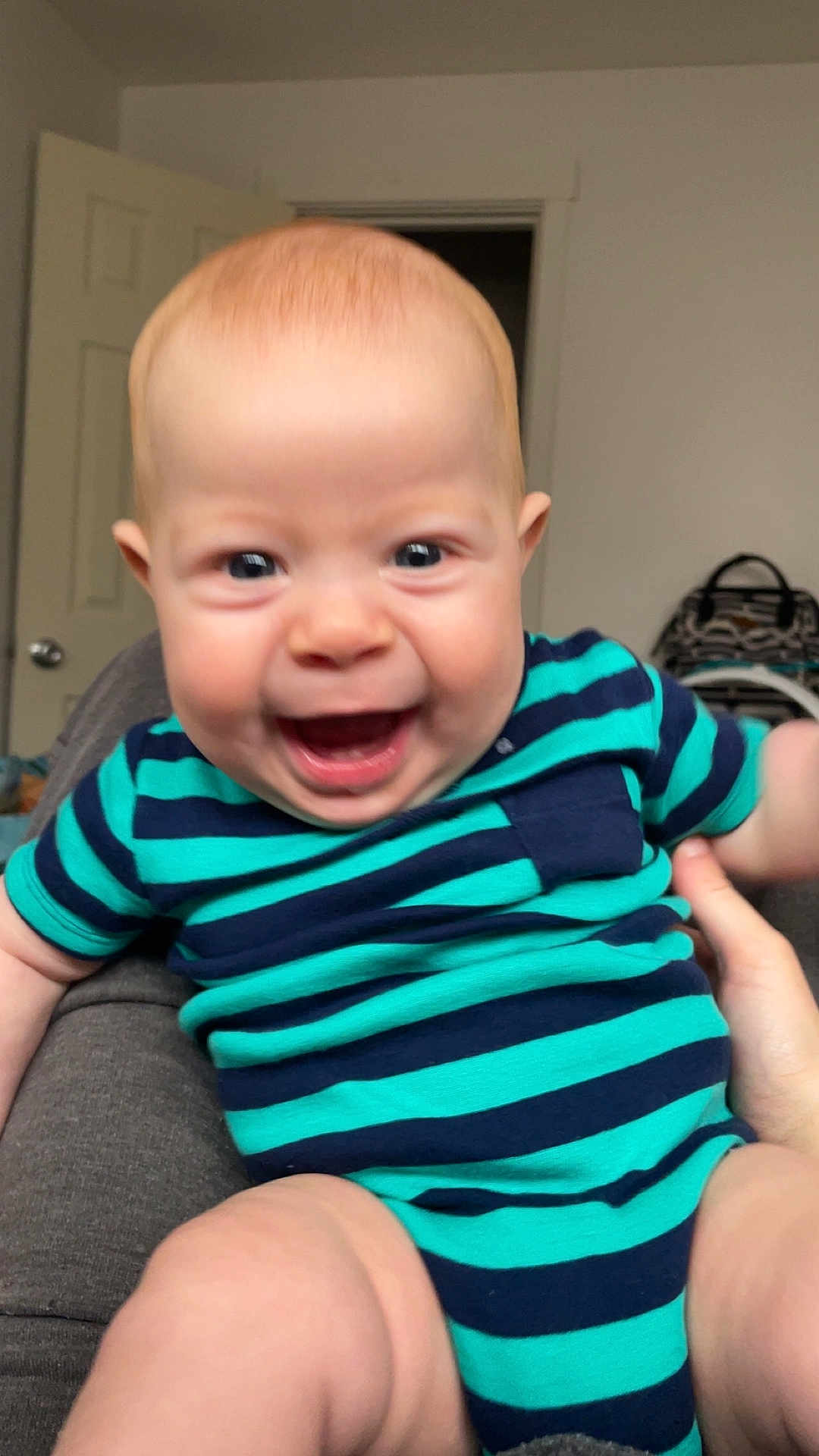 Colter joined the competition — help win amazing prizes! baby, child, smiling, indoor, person, clothing, striped_clothing, onesie, happy, face, head, skin, hand, leg, door, furniture, room, background, blue, green