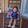 child, rocking_chair, american_flag, porch, patriotic_clothing, plaid_cushion, wooden_furniture, star_decorations, smiling, young_child, outdoor, summer, happy, casual, footwear, braided_hair, decor, wooden_floor, door, home