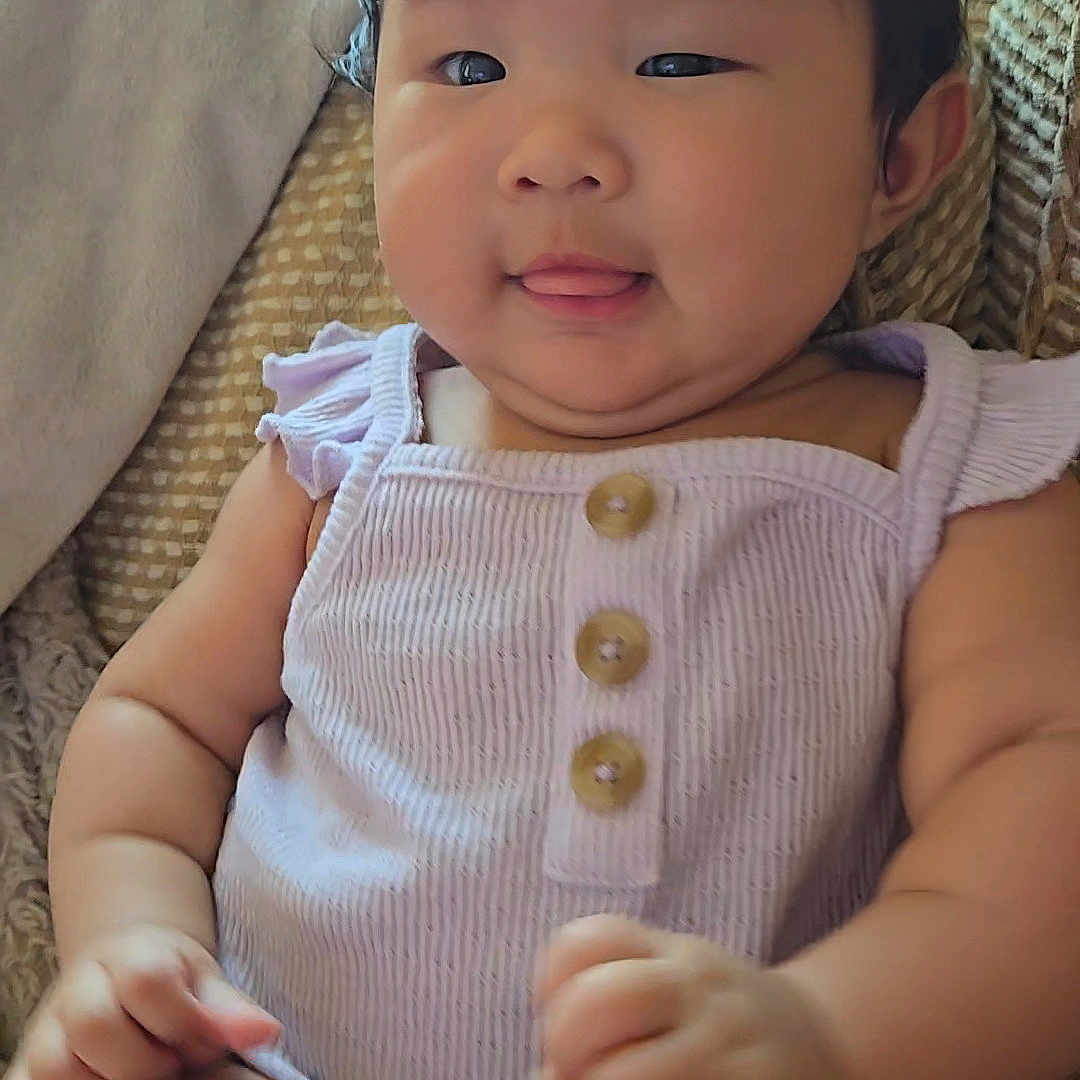 Thuy is registered to the contest to win money with this photo: arm, baby, child, chubby_cheeks, couch, cute, face, hand, indoor, infant, person, purple_clothing, romper, seat, skin, smiling, soft_light, textured_chair, tongue_out, wooden_buttons