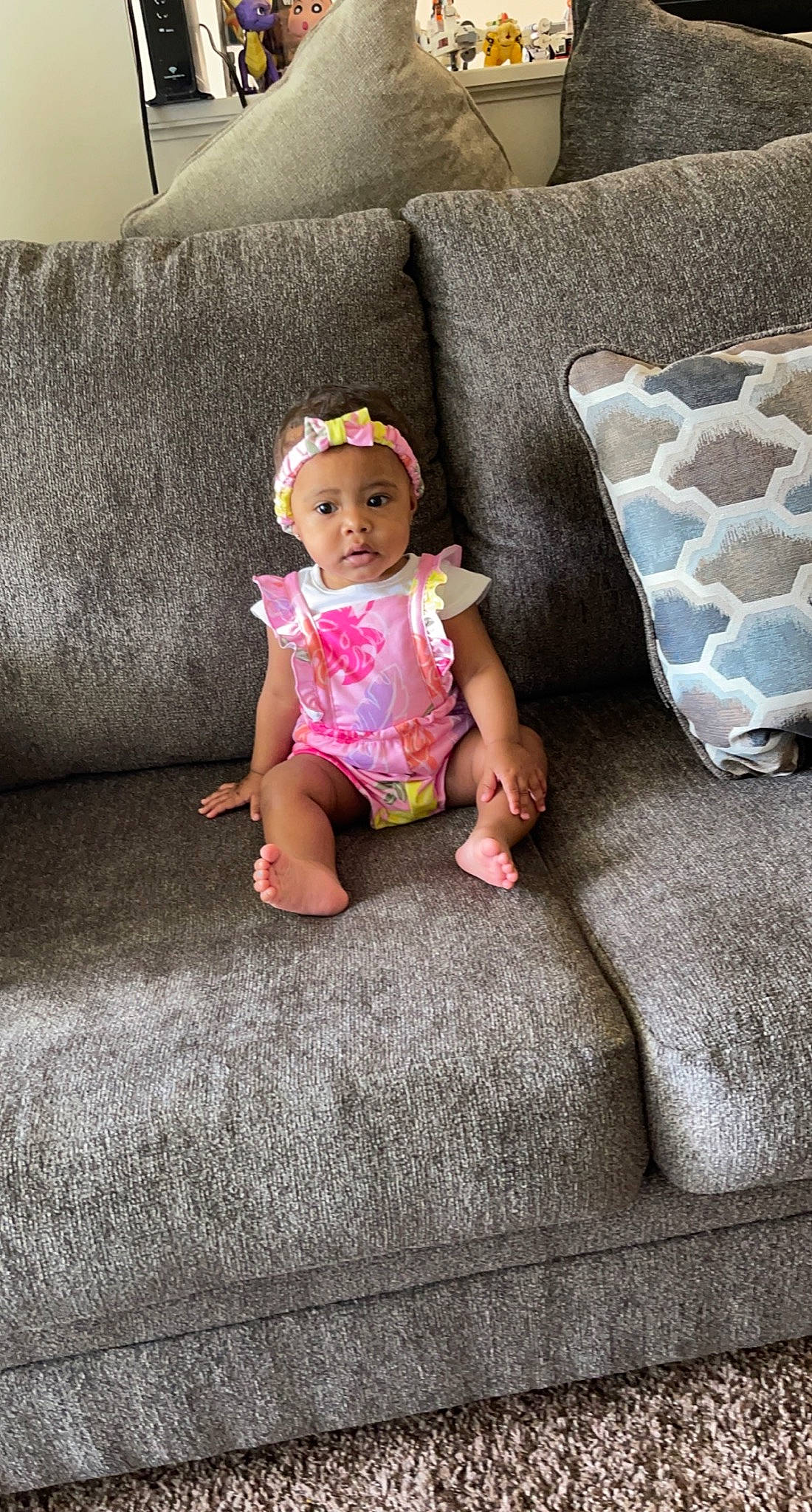 Nyasia is registered to the contest to win money with this photo: baby, baby_toddler_clothing, child, comfort, couch, floor, flooring, grass, grey, headwear, leg, linens, living_room, pattern, person, pillow, skin, sleeve, t_shirt, textile