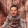 baby, boy, smiling, portrait, vest, bow_tie, button_up_shirt, sitting, wooden_background, happy, child, cute, fashion, formal_wear, indoor, young_child, face, hands, eyes, hair