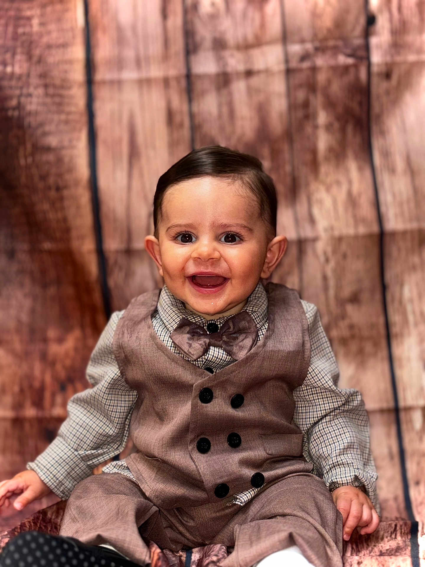 Benjamin a rejoint le concours — aidez-le/la à gagner de superbes lots ! baby, boy, smiling, portrait, vest, bow_tie, button_up_shirt, sitting, wooden_background, happy, child, cute, fashion, formal_wear, indoor, young_child, face, hands, eyes, hair