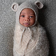 Elijah joined the competition — help win amazing prizes! baby, infant, swaddled, knit_hat, bear_ears, fuzzy_wrap, cute, portrait, looking_at_camera, face, newborn, soft_texture, cozy, lying_down, gray_background, closeup, child, adorable, warm_clothing, indoor