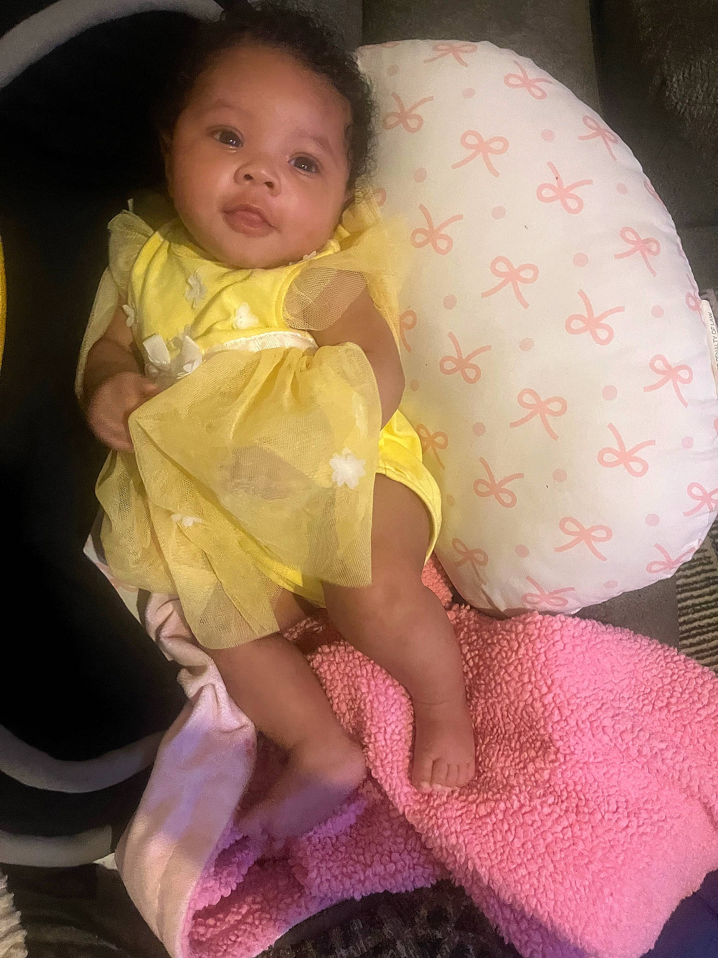 apparel, baby, blanket, child, comfort, cute, fabric, face, feet, indoors, infant, legs, lying_down, pattern, pillow, pink_blanket, rest, smile, soft_toys, yellow_dress