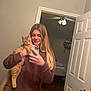 Butters joined the competition — help win amazing prizes! woman, cat, mirror, selfie, bathroom, sink, toiletries, phone, long_hair, orange_cat, sweatshirt, bedroom, ceiling_fan, door, smile, reflection, countertop, brush, bottle, casual