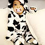 Uhaina Joyaux Mboyo a rejoint le concours — aidez-le/la à gagner de superbes lots ! baby, child, cow_print, onesie, pacifier, hood, horns, couch, pillows, soft_toys, indoor, seated, cute, infant, cozy, apparel, black_and_white, face, expression, comfort