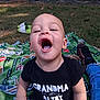 Omari is registered to the contest to win money with this photo: toddler, child, smiling, outdoor, grass, blanket, shirt, text_on_clothing, trees, footwear, sock, jeans, playful, happy, person, nature, daylight, expression, sitting, park