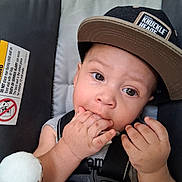 Omari is registered to the contest to win money with this photo: baby, child, cap, hat, car_seat, safety_harness, plush_toy, stuffed_animal, hand, fingers, face, eyes, infant, seat, clothing, cute, indoors, expression, person, young