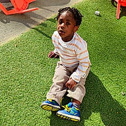 Jezréel-Kendy a rejoint le concours — aidez-le/la à gagner de superbes lots ! child, boy, outdoor, grass, toy, plastic_chair, braided_hair, striped_shirt, shoes, playground, sunlight, shadow, sitting, curious, casual_clothing, beige_pants, blue_shoes, playtime, daylight, greenery