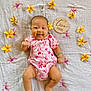 baby, infant, smiling, flower, pink_outfit, blanket, wooden_sign, two_months, cute, lying_down, happy, skin, hand, foot, floral_pattern, accessory, bracelet, indoors, portrait, child
