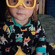 Kingston is registered to the contest to win money with this photo: child, toddler, yellow_goggles, toy_drill, pajamas, indoor, sitting, curious, colorful_clothing, face, hair, furniture, couch, play, expression, person, cute, young_child, home, portrait
