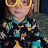 child, toddler, yellow_goggles, toy_drill, pajamas, indoor, sitting, curious, colorful_clothing, face, hair, furniture, couch, play, expression, person, cute, young_child, home, portrait