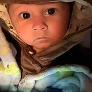 Xzavier is registered to the contest to win money with this photo: baby, infant, child, hooded_jacket, animal_hood, blanket, mobile_phone, phone_screen, cartoon_on_screen, close_up, portrait, big_eyes, serious_expression, cozy, soft_light, brown_color, plush, clothing, indoor, adorable
