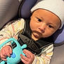 baby, infant, newborn, car_seat, seat_belt, buckle, beanie, hat, toy, silicone_toy, hand, onesie, striped_clothing, close_up, portrait, indoor, fabric, warning_label, seat_cushion, strapped